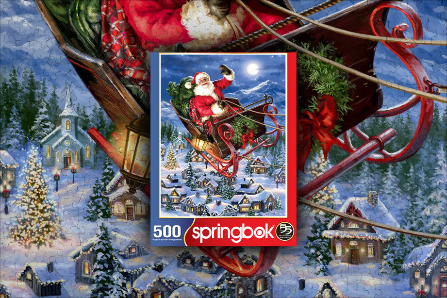 Box and Finished Puzzle of Delivering Christmas puzzle featuring Santa flying in his sleigh over a snowy village by Springbok