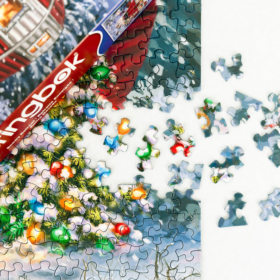 box and pieces from Snowy Retreat puzzle featuring a festive red camper with Christmas lights in a snowy forest by Springbok